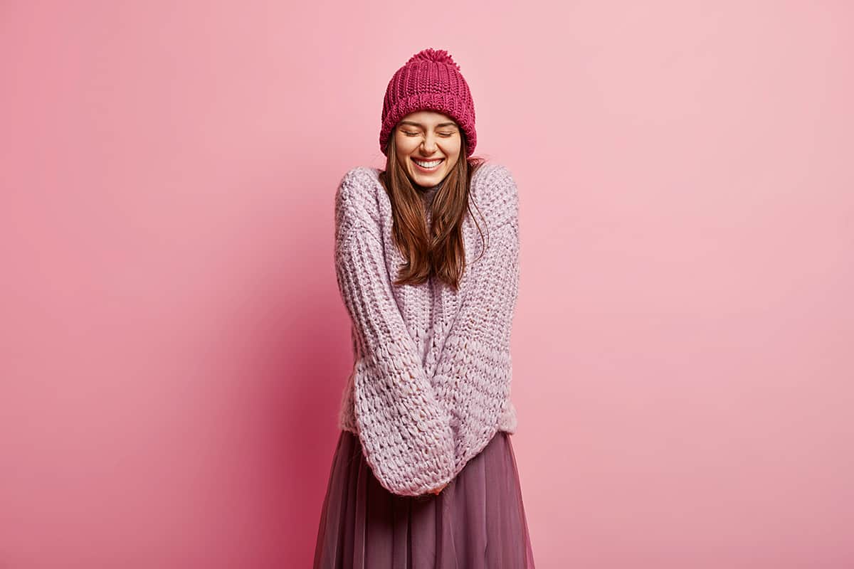 Frau mit Wollpulli und Wollmütze vor rosa Hintergrund